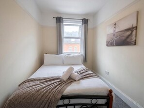 A bedroom with a bed, a window with curtains, a painting on the wall, and a view of a building outside. - Stylish 3-bed Apartment - Caterham - Sleeps 5 (Caterham)