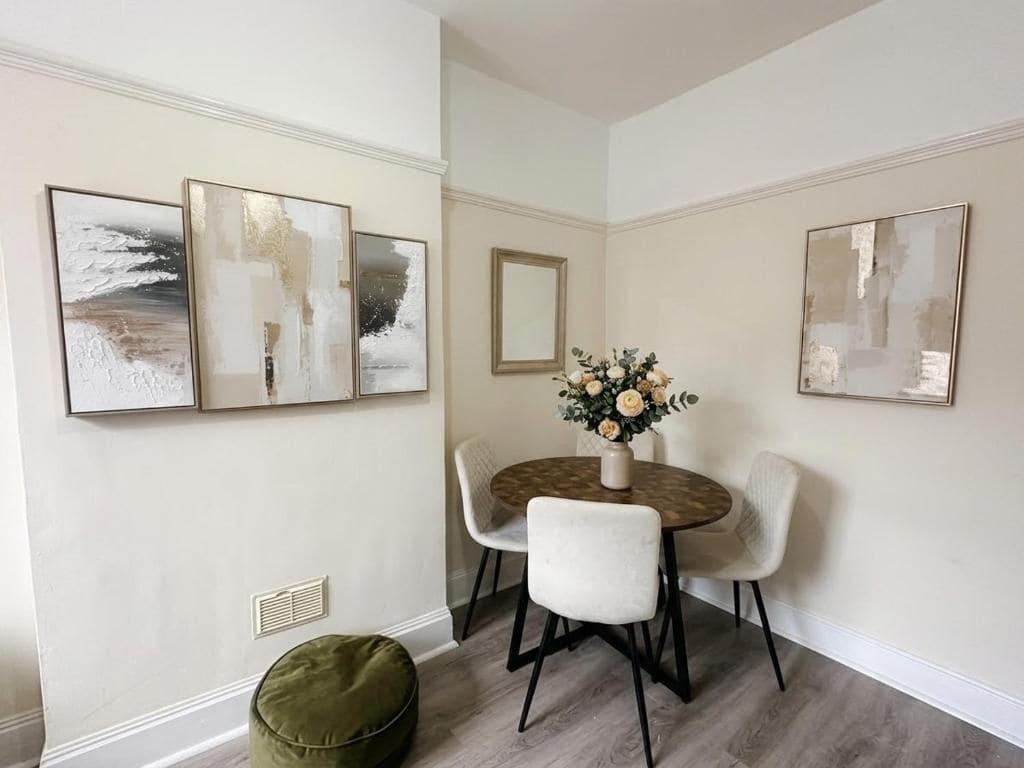 A dining area with a round table, four chairs, and three wall-mounted abstract paintings.