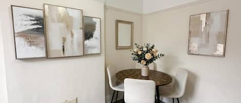 A dining area with a round table, four chairs, and three wall-mounted abstract paintings.