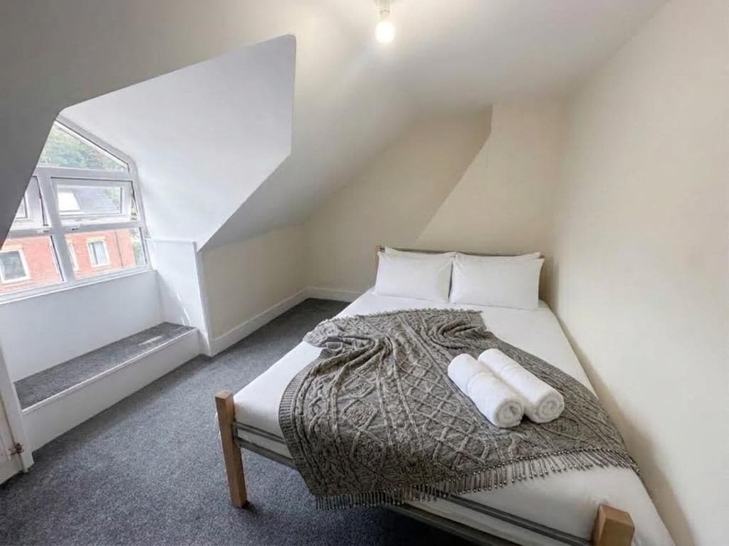 A bedroom with a sloped ceiling, a bed with a patterned blanket, and a window overlooking a building.