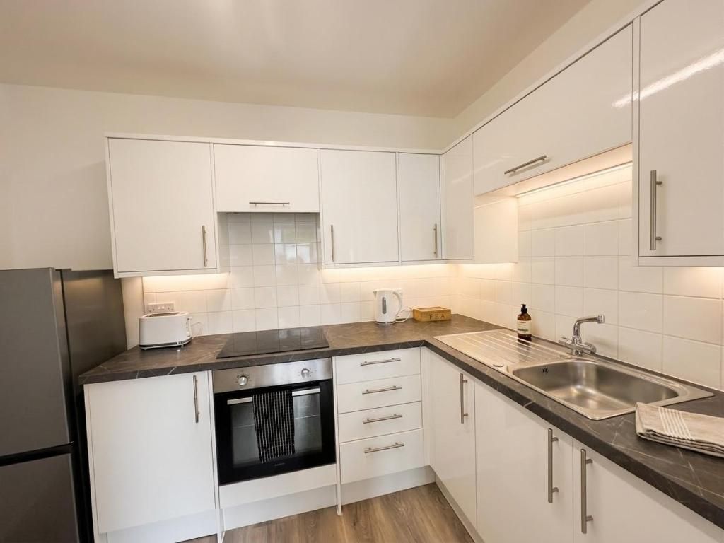 A modern kitchen with white cabinets, a built-in oven, a stainless steel sink, and a marble countertop.