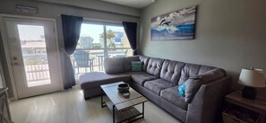 A living room with a grey sofa, a small table, a lamp, and a painting of dolphins on the wall. - Hidden Gem One of Port A’s best-kept secrets (Port Aransas)