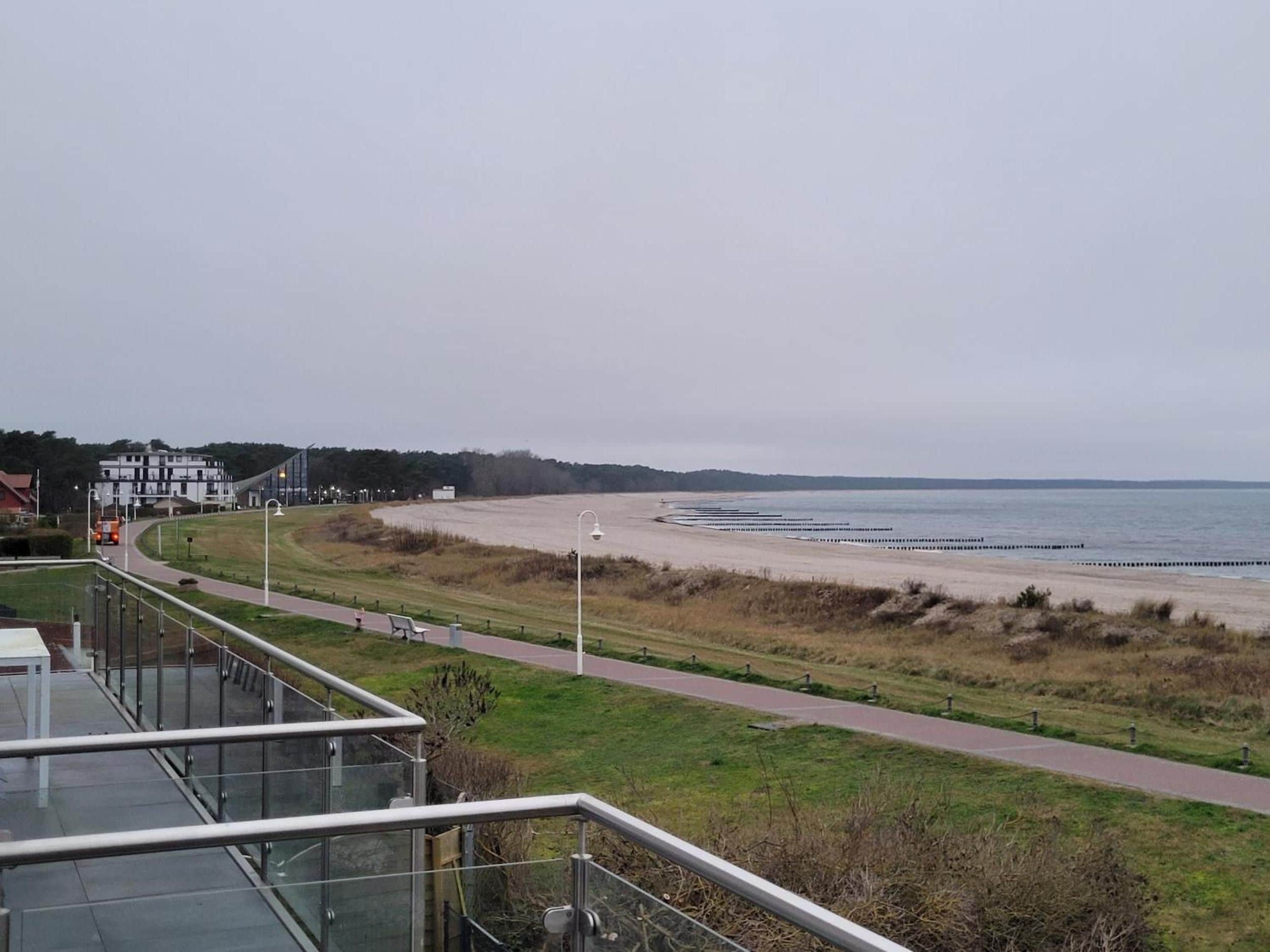 Une vue sur la côte, avec une promenade dallée, une plage et un bâtiment en arrière-plan.