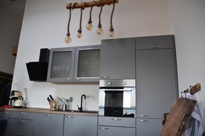 A modern kitchen with grey cabinets, a built-in oven, and a hanging light fixture with clear glass bulbs.