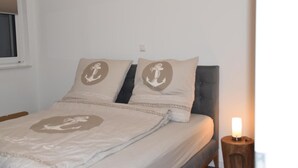 Ein Bett mit zwei Kissen, ein Nachttisch mit Lampe und ein Fenster mit Jalousie.