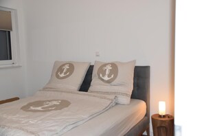 Una cama con dos almohadas, una mesita de noche con una lámpara y una ventana con cortina.