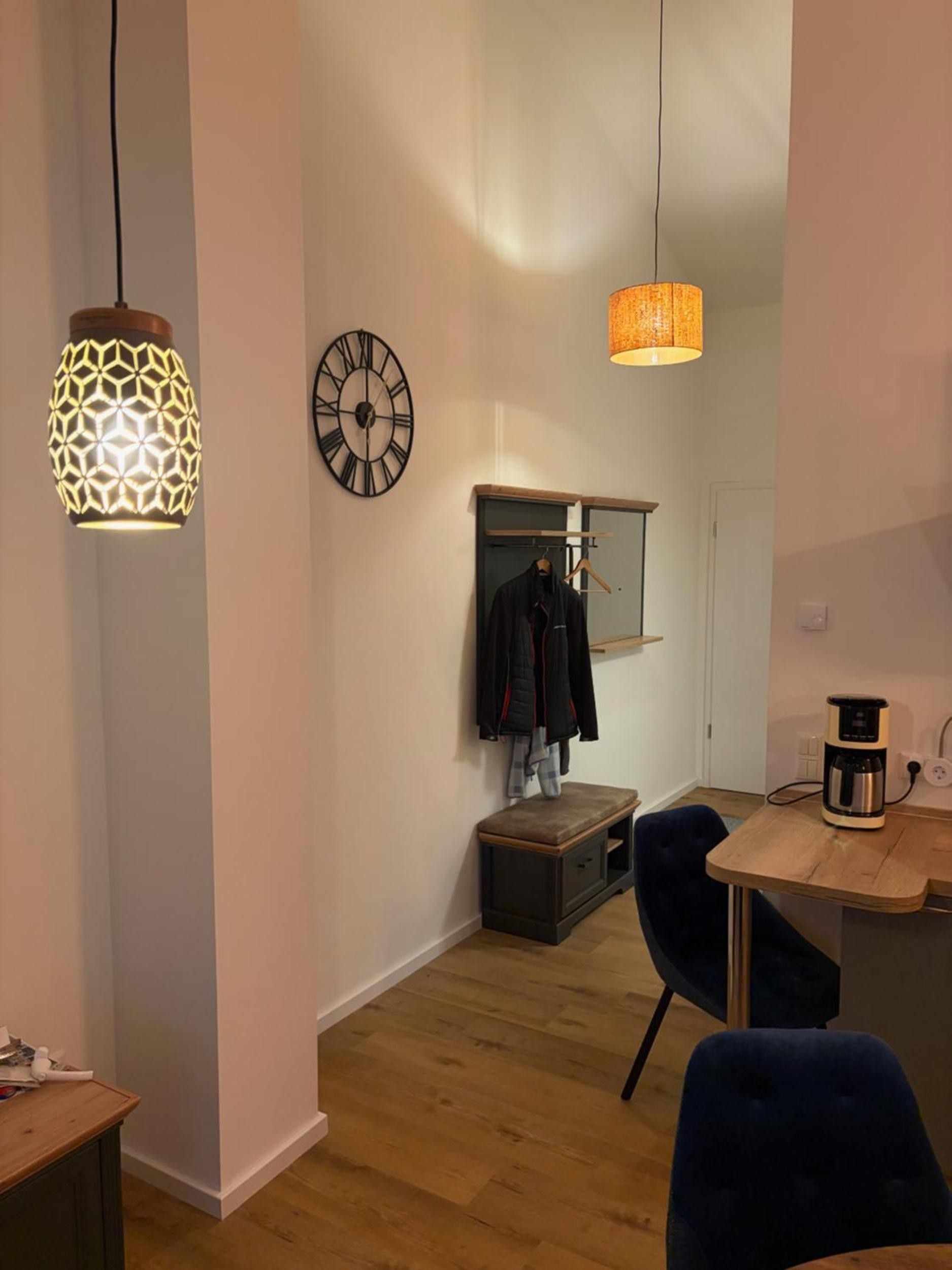 Ein modernes Interieur mit einer Holzbank, einem Kleiderhaken, einer Uhr und Pendelleuchten.