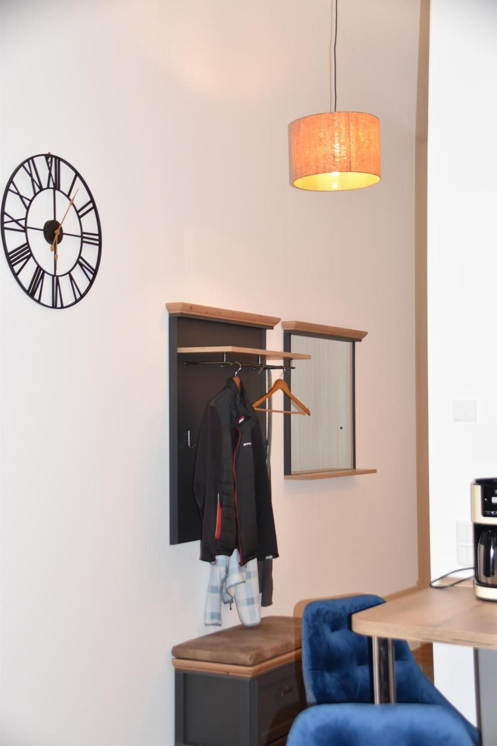 Une pièce comprenant une horloge, un porte-manteau suspendu, un miroir, une table en bois et une chaise bleue.