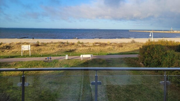 Blick auf die Küste mit Strand, Leuchtturm und einer Wiese mit einem Schild.