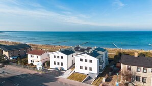 Ein Küstenwohngebiet mit modernen weißen Häusern, freiem Blick auf das Meer und einem Sandstrand mit einem Steg.