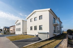 A modern residential building with a flat roof, multiple windows, and a balcony.
