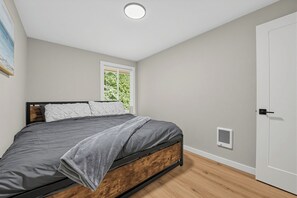 Ett sovrum med en säng, ett fönster, en dörr och en väggmonterad ventilationsöppning.
