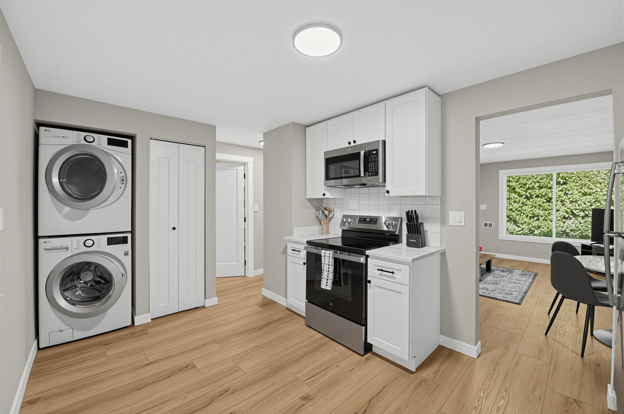 A modern kitchen with built-in appliances, a dining area, and a view of greenery outside.