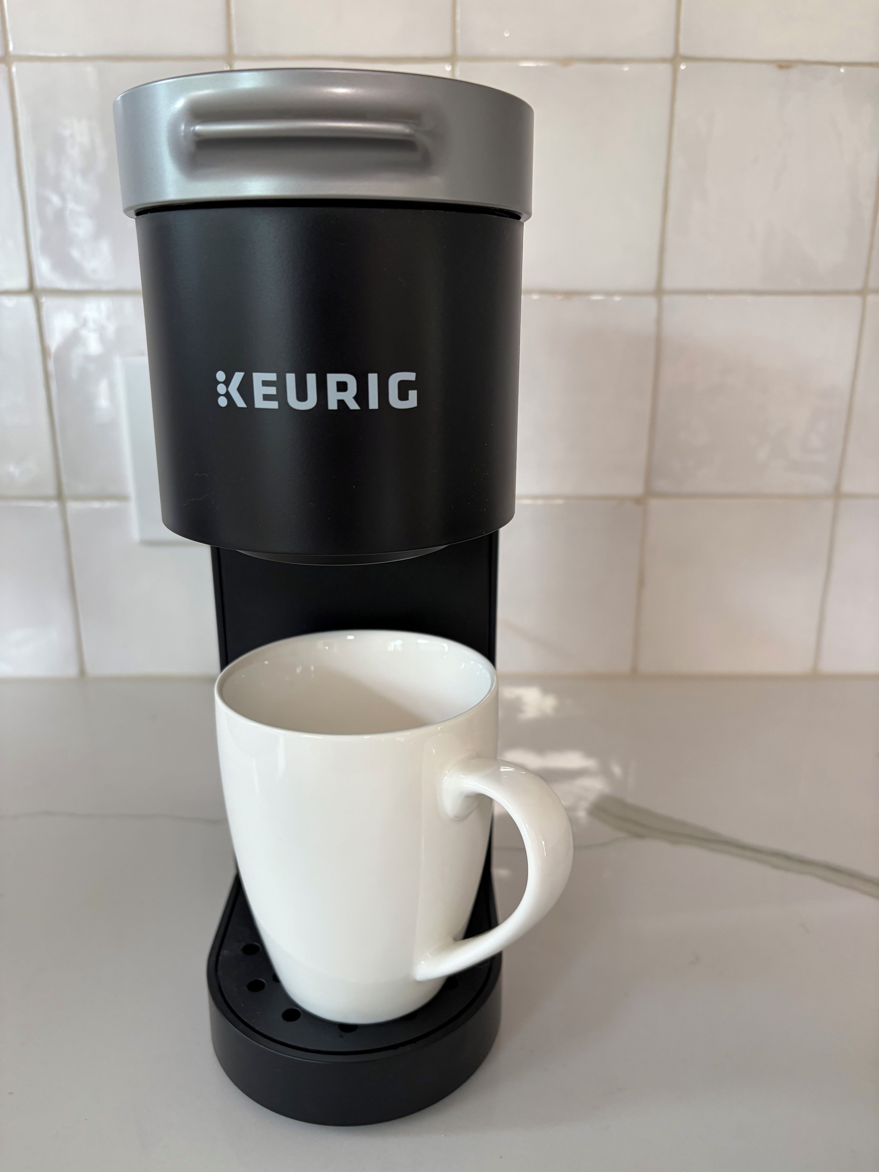 Eine Keurig-Kaffeemaschine mit einer weißen Tasse auf dem Sockel.