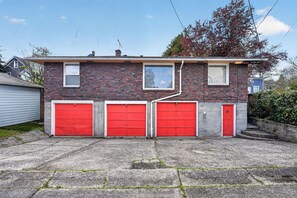 Una casa de ladrillo de dos pisos con tres puertas de garaje rojas y un pequeño porche delantero.