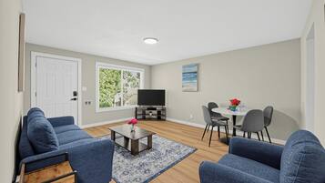 A living room with a TV, sofa, coffee table, and dining area with chairs.
