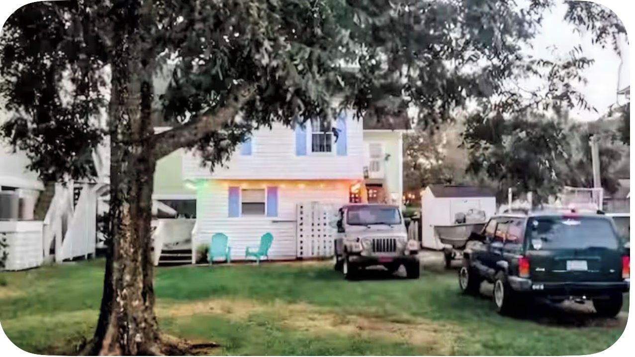 Un quartier résidentiel avec une maison blanche, un arbre et des véhicules garés.