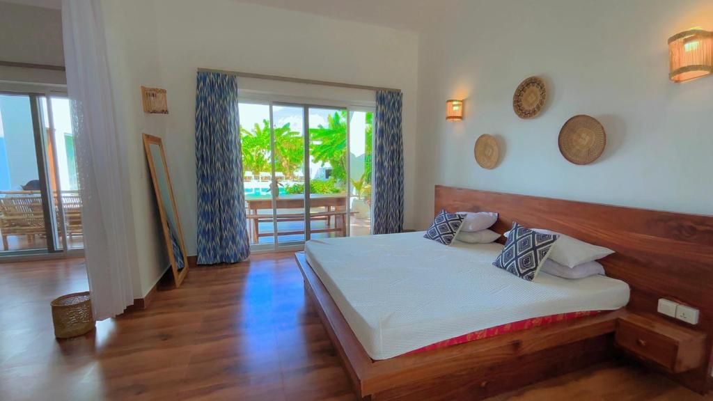 Un dormitorio con una cama grande, cabecera de madera y vistas a una piscina y palmeras a través de un ventanal corredero.