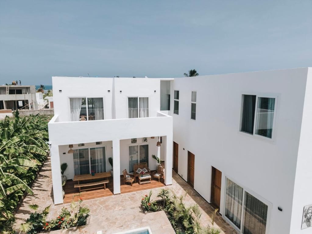 Un bâtiment moderne de couleur blanche, doté d’un patio, d’un espace extérieur aménagé avec des sièges et d’une piscine.