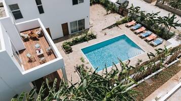 A modern building with a rooftop patio, a swimming pool, and lounge chairs.