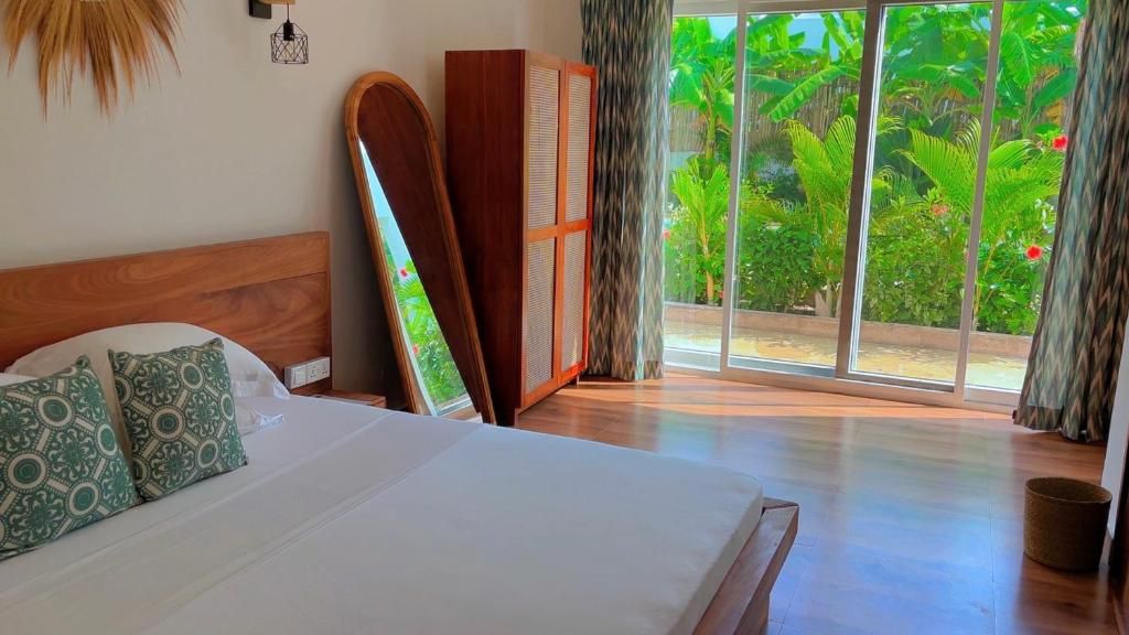 A bedroom with a large bed, a wooden wardrobe, and a view of lush greenery through a sliding glass door.