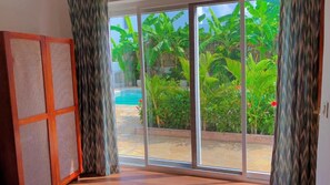 Una habitación con puerta corrediza de vidrio que da a un área de piscina con abundante vegetación.