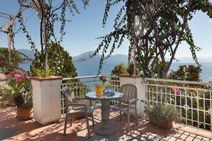 An outdoor seating area with a table and chairs, overlooking a body of water and mountains.