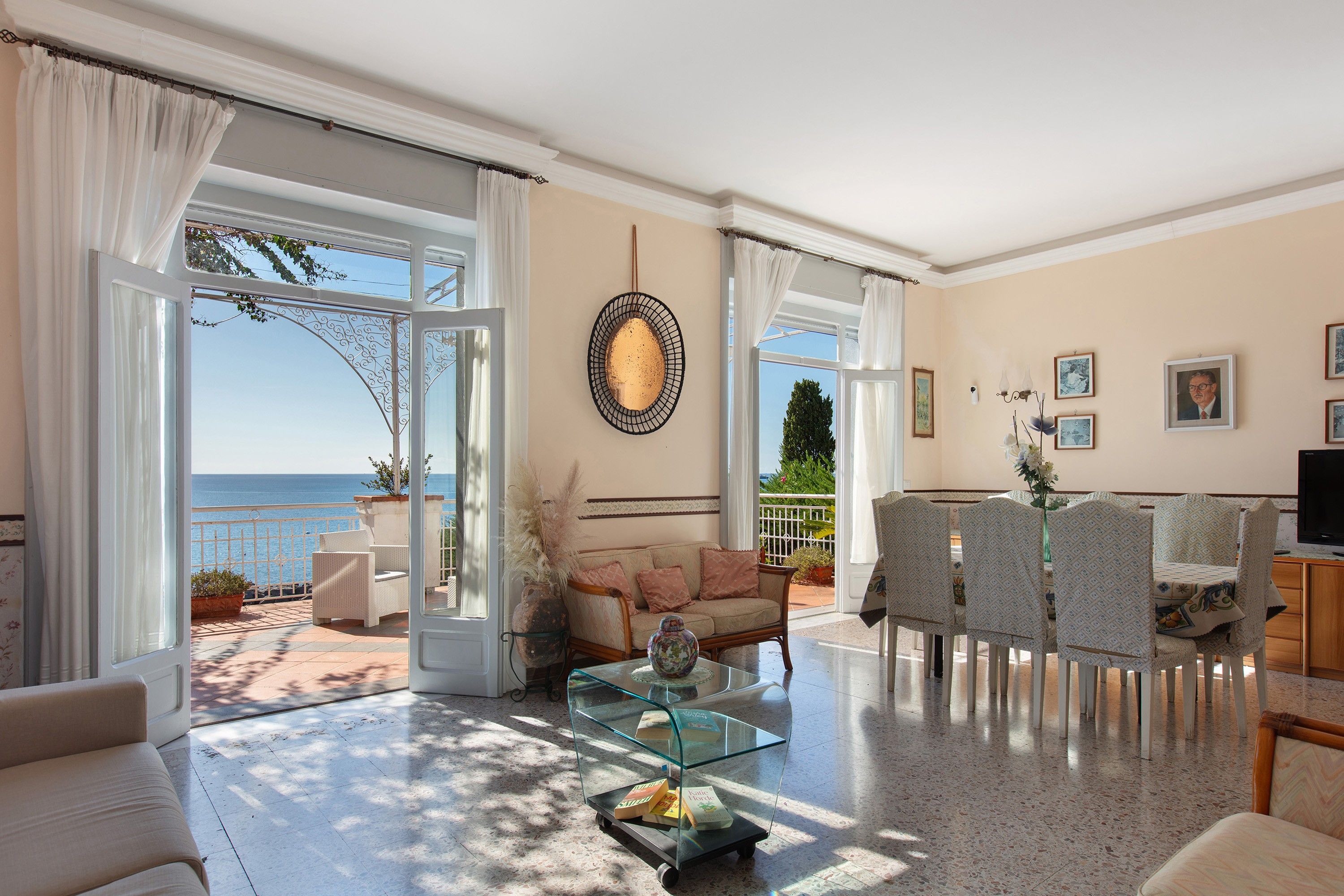 A spacious living room with a view of the sea, a glass coffee table, and a sofa.