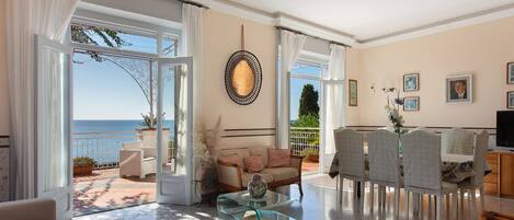 A spacious living room with a view of the sea, a glass coffee table, and a sofa.