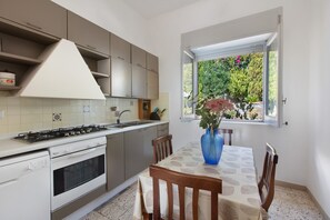 A kitchen with a gas stove, oven, and a dining area with a table and chairs. - Villa Scogliera dei Gabbiani with sea view, shared pool and Wi-Fi (Scario)