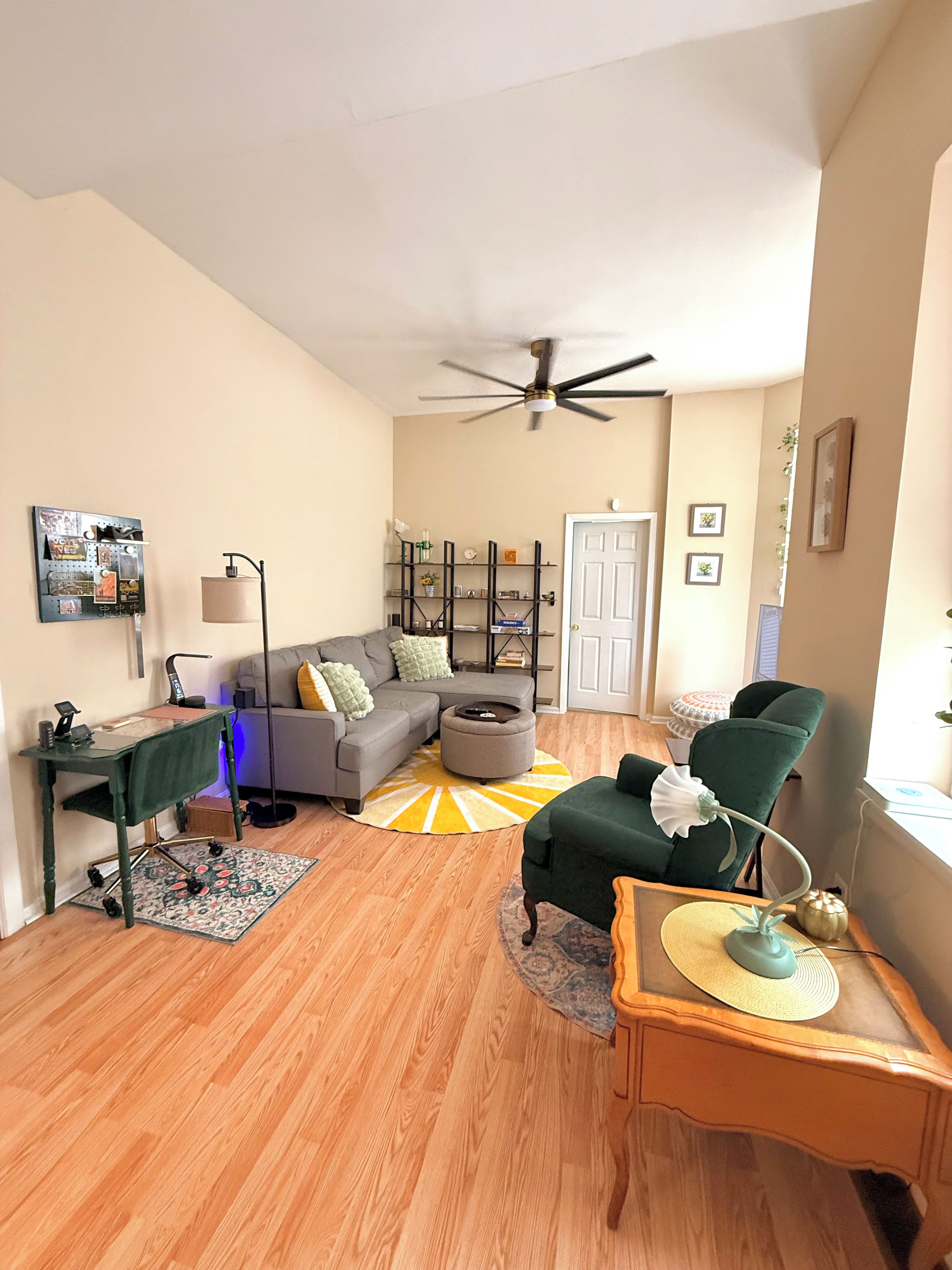 A living room with a sofa, ottoman, coffee table, and a desk with a lamp.