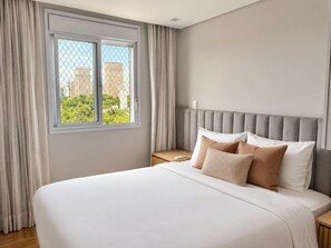 A hotel room with a large bed, a nightstand, a window with curtains, and a view of buildings outside. - You Faria Lima (São Paulo)