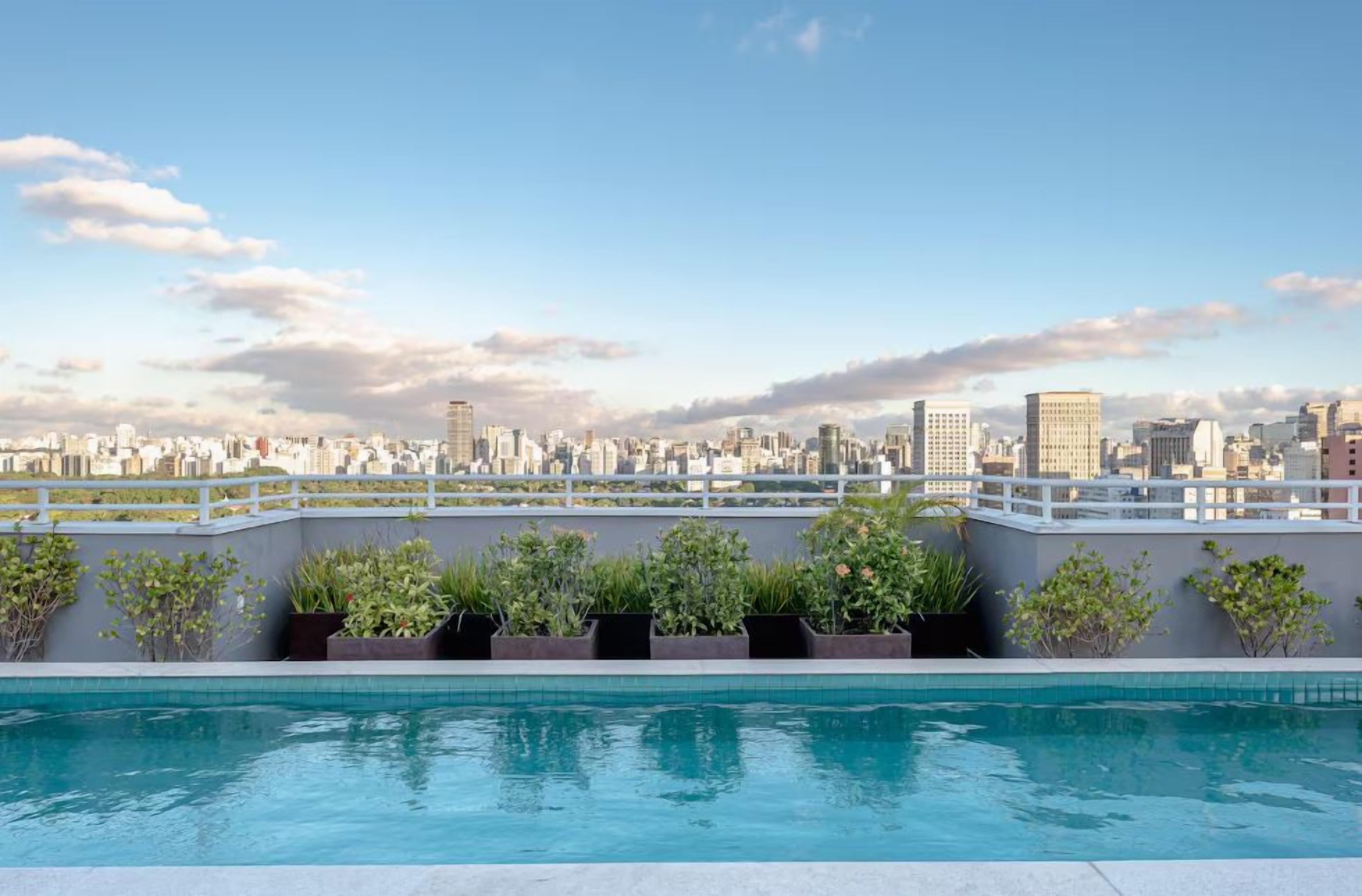 A rooftop swimming pool with a cityscape view, surrounded by planters and a white railing.
