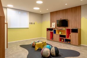 A room with a television mounted on the wall, a play area with colorful balls, and a bookshelf with toys. - You Faria Lima (São Paulo)
