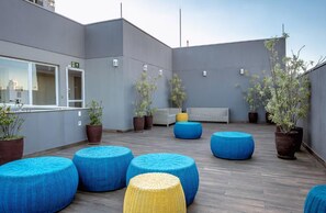 A rooftop terrace with blue and yellow woven seating, potted plants, and a white bench. - You Faria Lima (São Paulo)