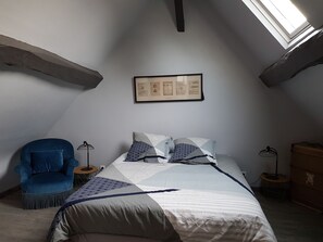 A bedroom with a sloped ceiling, a bed with patterned bedding, a blue armchair, and a framed picture on the wall. - "First Floor" Apartment with Shared Garden, Wi-Fi, and Air Conditioning (Saint-Germain-sur-Avre)