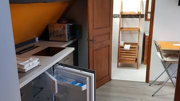 A compact kitchen with a refrigerator, microwave, and wooden cabinets. A skylight provides natural light, and a wooden door leads to a dining area.