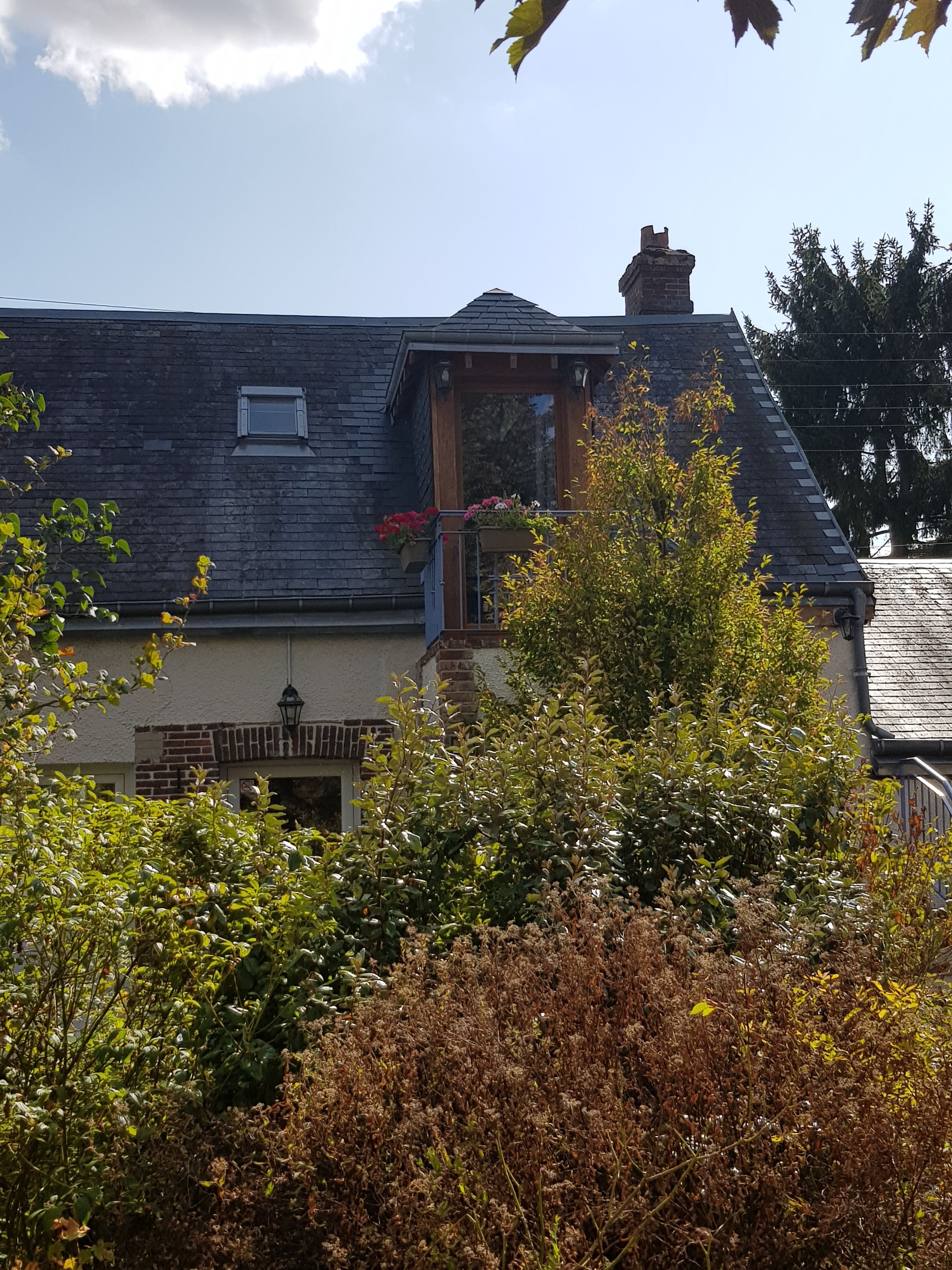 A house with a sloped roof, a visible chimney, and a small balcony with flowers.