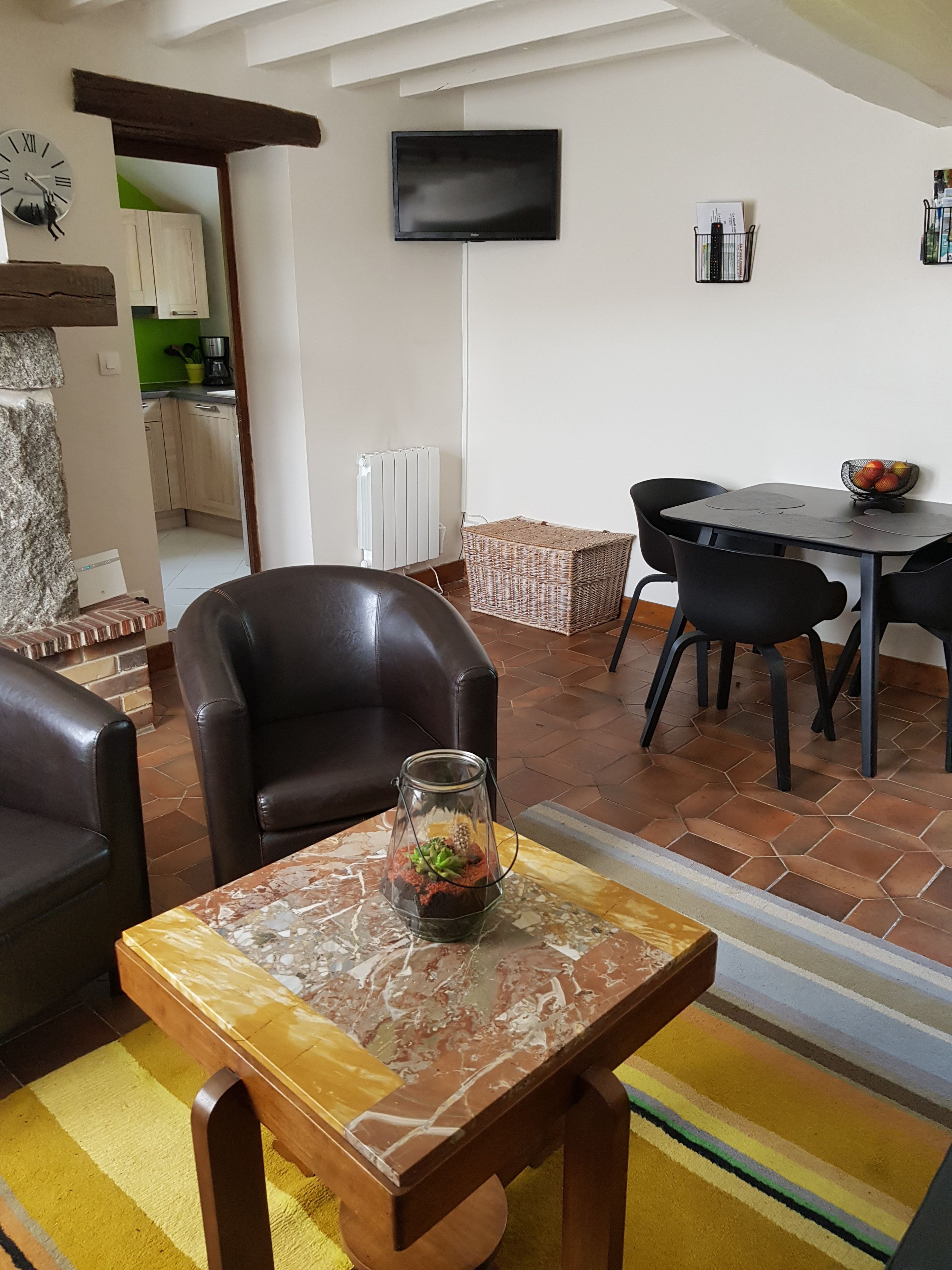 Un salon avec un téléviseur fixé au mur, un coin repas avec une table et des chaises, et une cuisine visible au fond.