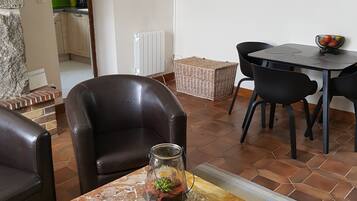 A living room with a TV mounted on the wall, a dining area with a table and chairs, and a kitchen visible in the background.