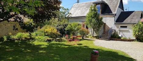Ein Steinhaus mit geneigtem Dach, einer Schotterauffahrt und einem kleinen Garten mit einer Bank und einem Blumentopf.