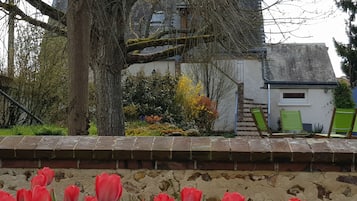 Een tuin met rode tulpen, een boom en een gebouw met een stenen muur.