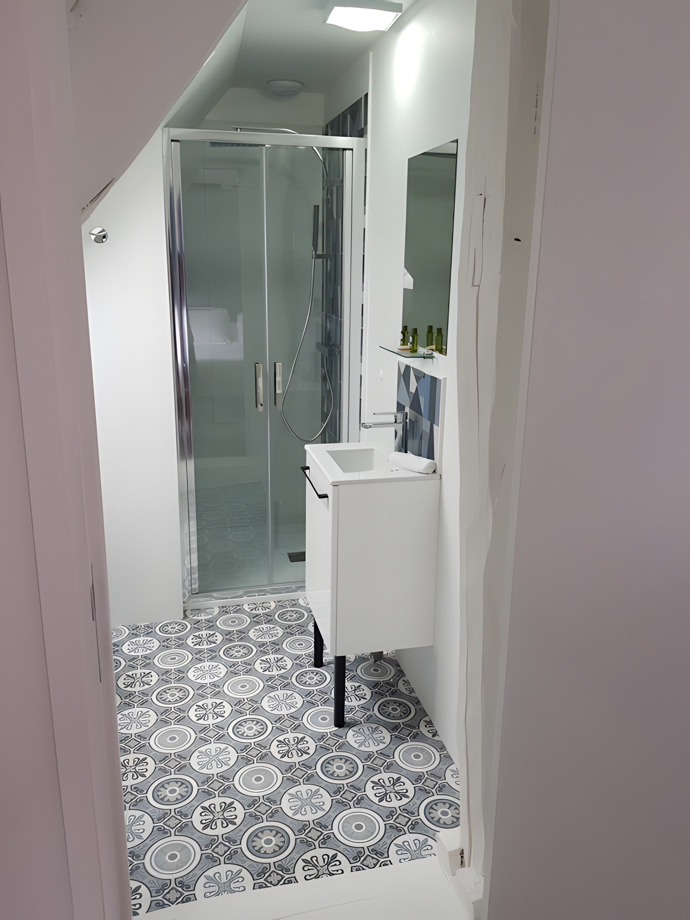Une salle de bain moderne avec une douche à parois de verre, un lavabo blanc et des carreaux de sol à motifs.