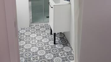 Une salle de bain moderne avec une douche à parois de verre, un lavabo blanc et des carreaux de sol à motifs.