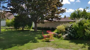 Un jardin avec un arbre, un chemin de gravier et une table et des chaises rouges.