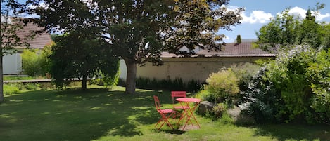A garden with a tree, a gravel path, and a red table and chairs.