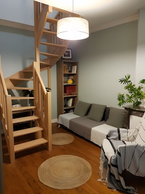 A room with a wooden staircase, a sofa, a bookshelf, and a hanging light fixture. - Guest Room "Chambre bleue - 1st Floor" with Shared Garden and Wi-Fi (Saint-Germain-sur-Avre)