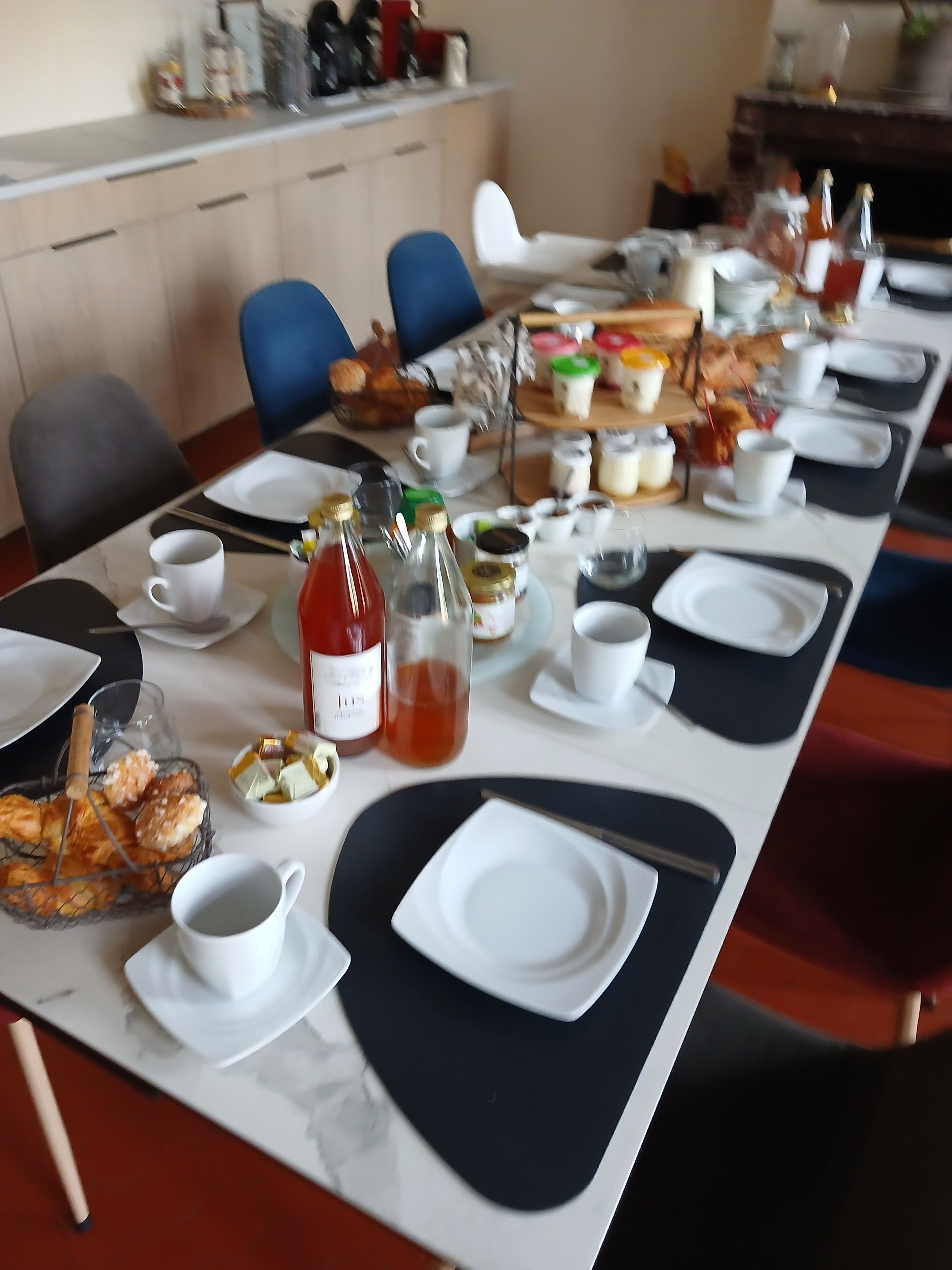 Une table à manger dressée avec des assiettes, des tasses et divers aliments, ce qui indique qu’un repas est en préparation.