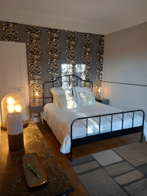 A bedroom with a metal bed frame, white bedding, a patterned wall, and a bedside lamp. - Guest Room "Chambre bleue - 1st Floor" with Shared Garden and Wi-Fi (Saint-Germain-sur-Avre)