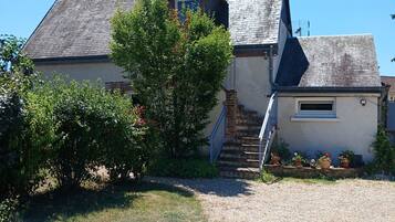 Une maison avec un toit en pente, une cheminée bien visible, une porte d’entrée et un petit escalier menant à l’entrée.